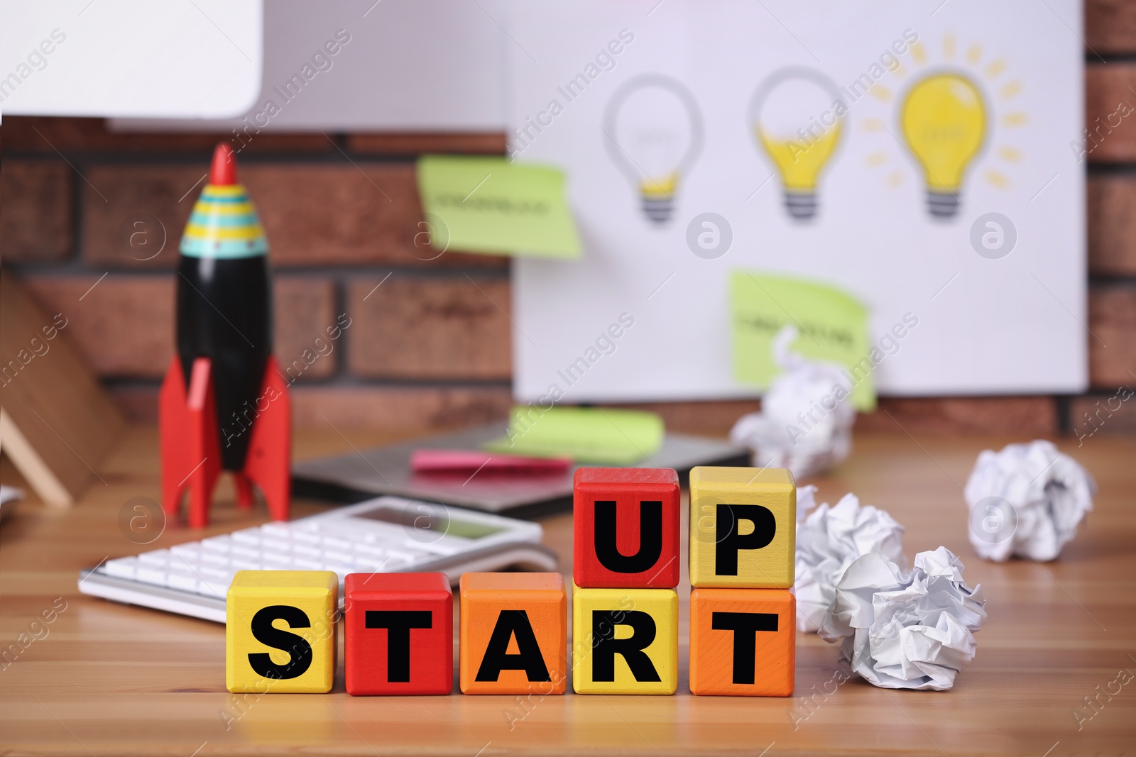 Photo of Colorful cubes with words Start Up and crumpled paper on wooden table indoors