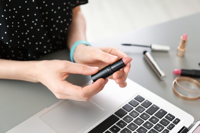 Young woman with makeup product using laptop at table. Beauty blogger