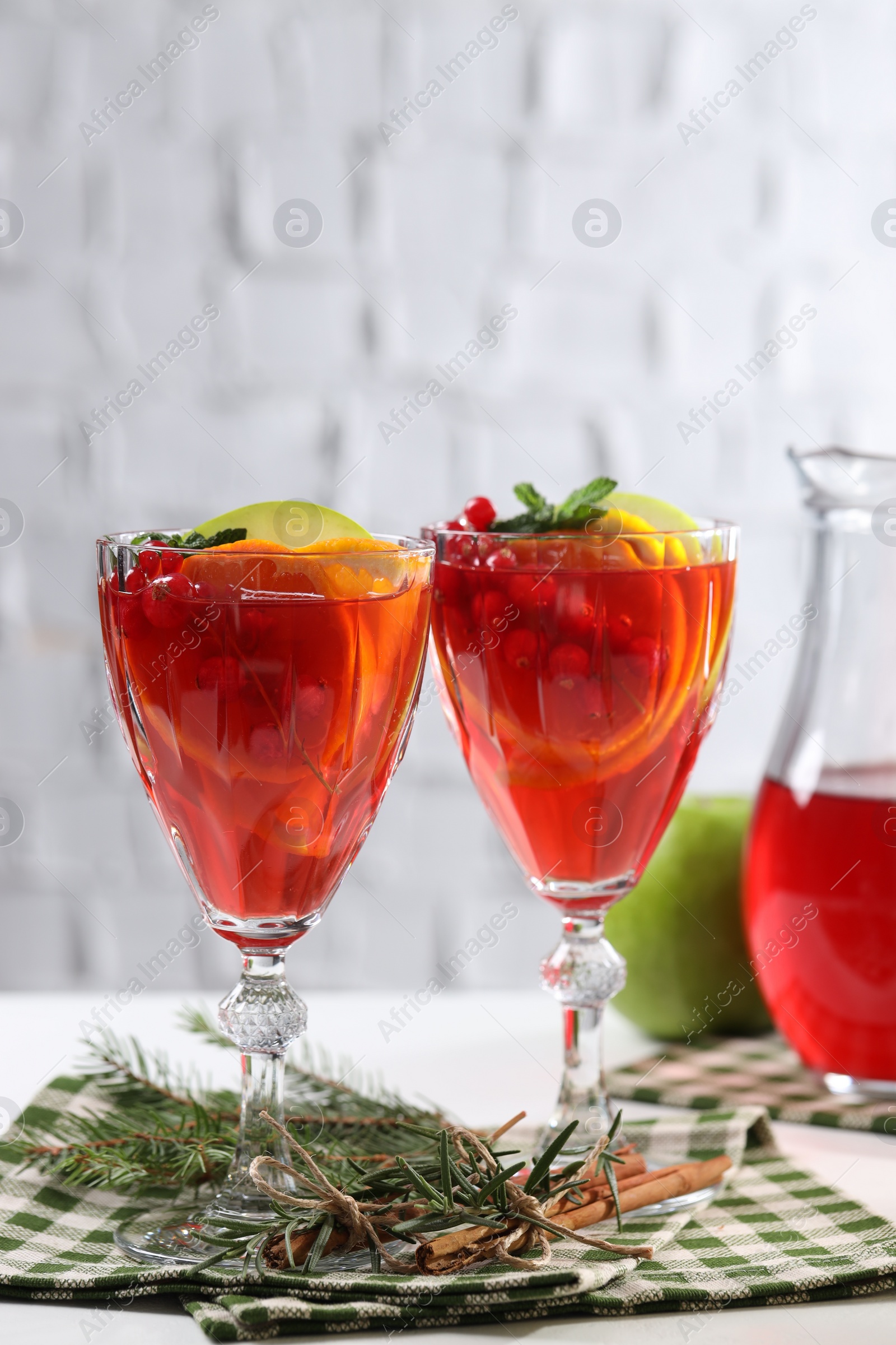 Photo of Christmas Sangria cocktail in glasses, cinnamon sticks and fir tree branch on white table against brick wall