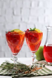 Photo of Christmas Sangria cocktail in glasses, cinnamon sticks and fir tree branch on white table against brick wall