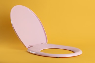 Photo of New pink plastic toilet seat on yellow background
