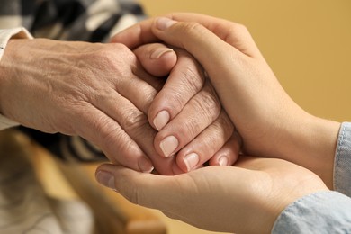 Photo of Young and elderly women holding hands on beige background, closeup