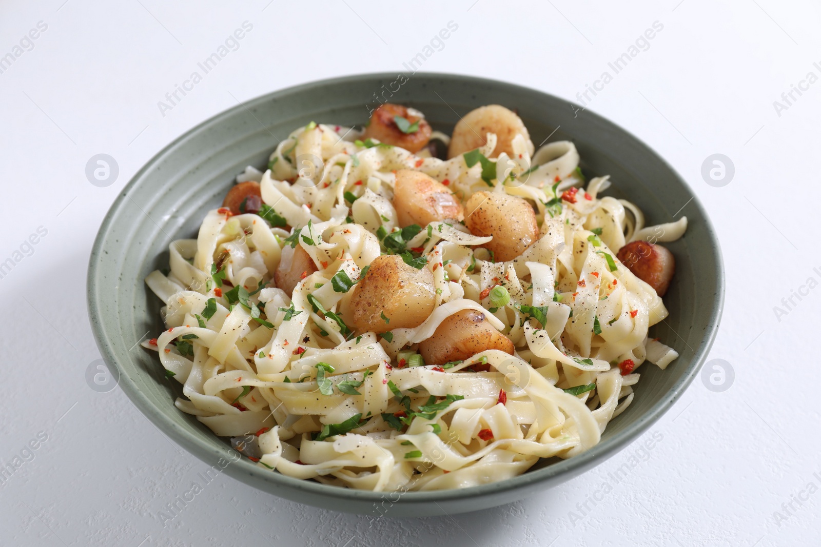 Photo of Delicious scallop pasta with spices in bowl on white table, closeup