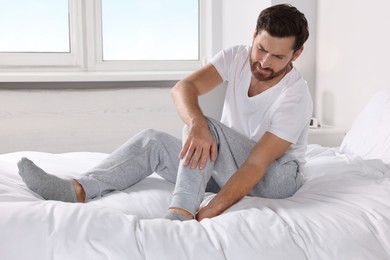 Photo of Man suffering from leg pain on bed at home