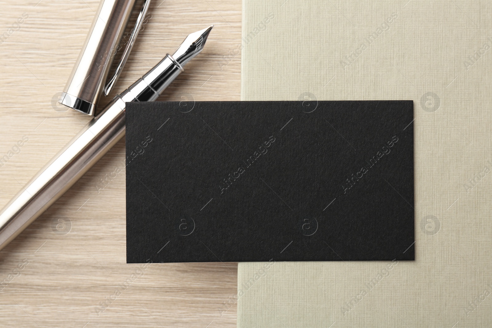 Photo of Blank black business card, fountain pen and notebook on wooden table, top view. Mockup for design