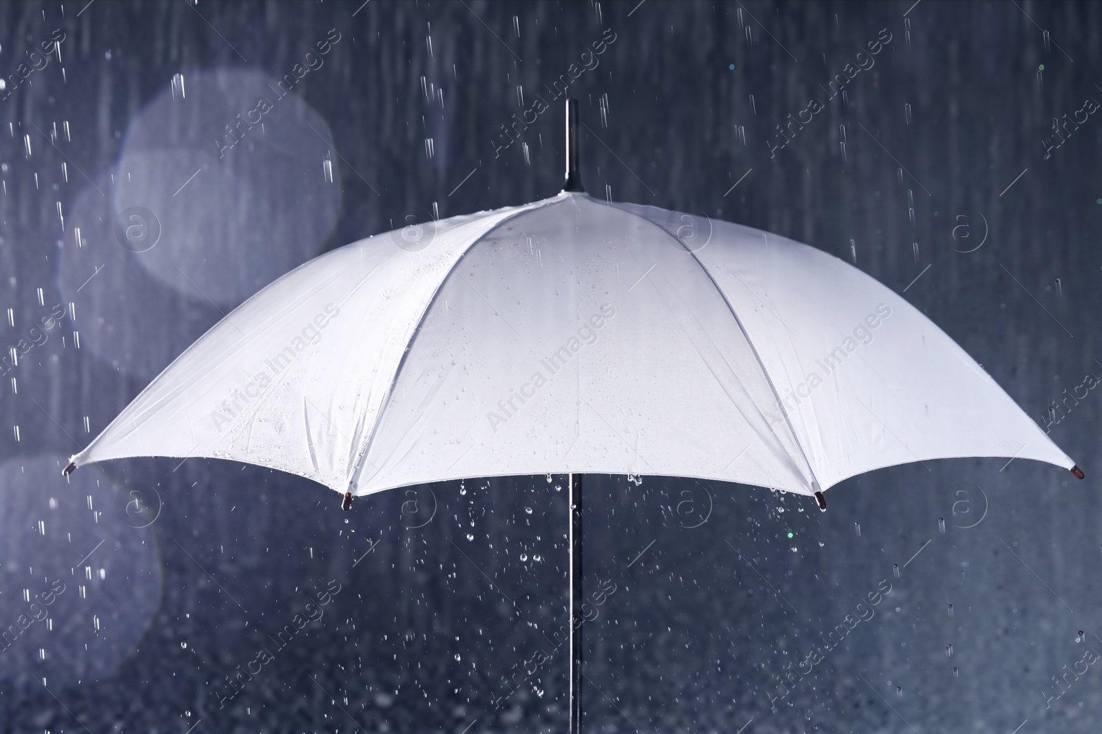 Photo of White umbrella under rain on dark background