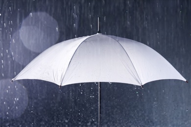 Photo of White umbrella under rain on dark background