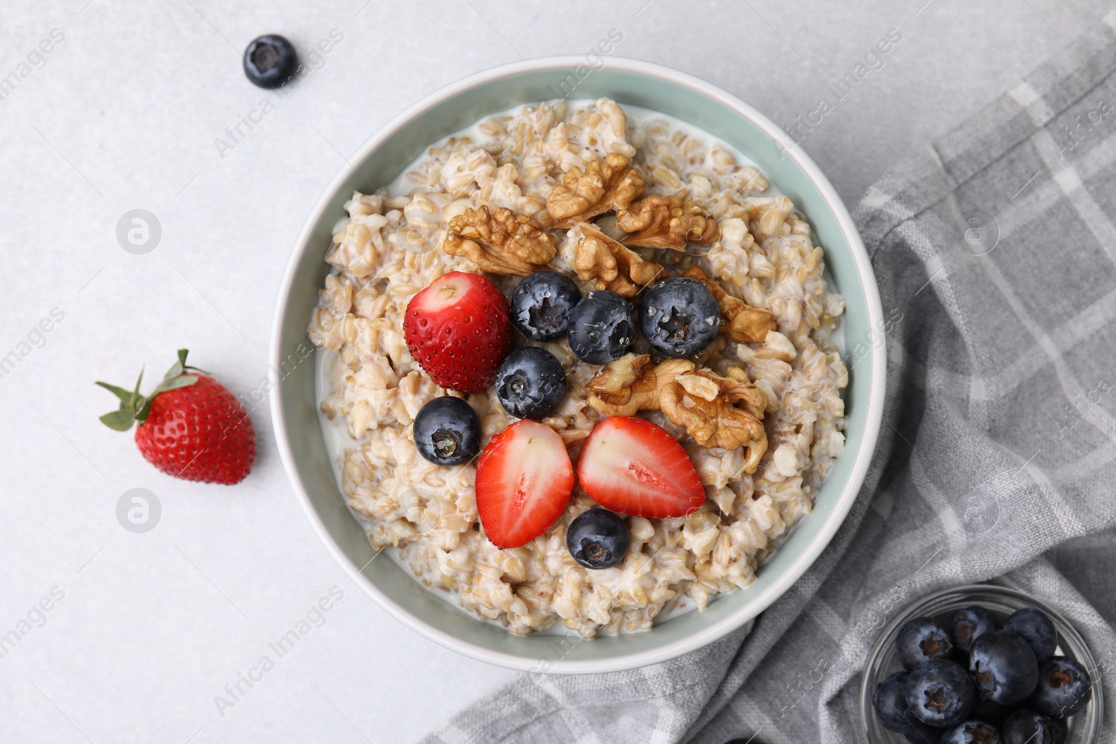 Photo of Tasty oatmeal with strawberries, blueberries and walnuts in bowl on grey table, flat lay