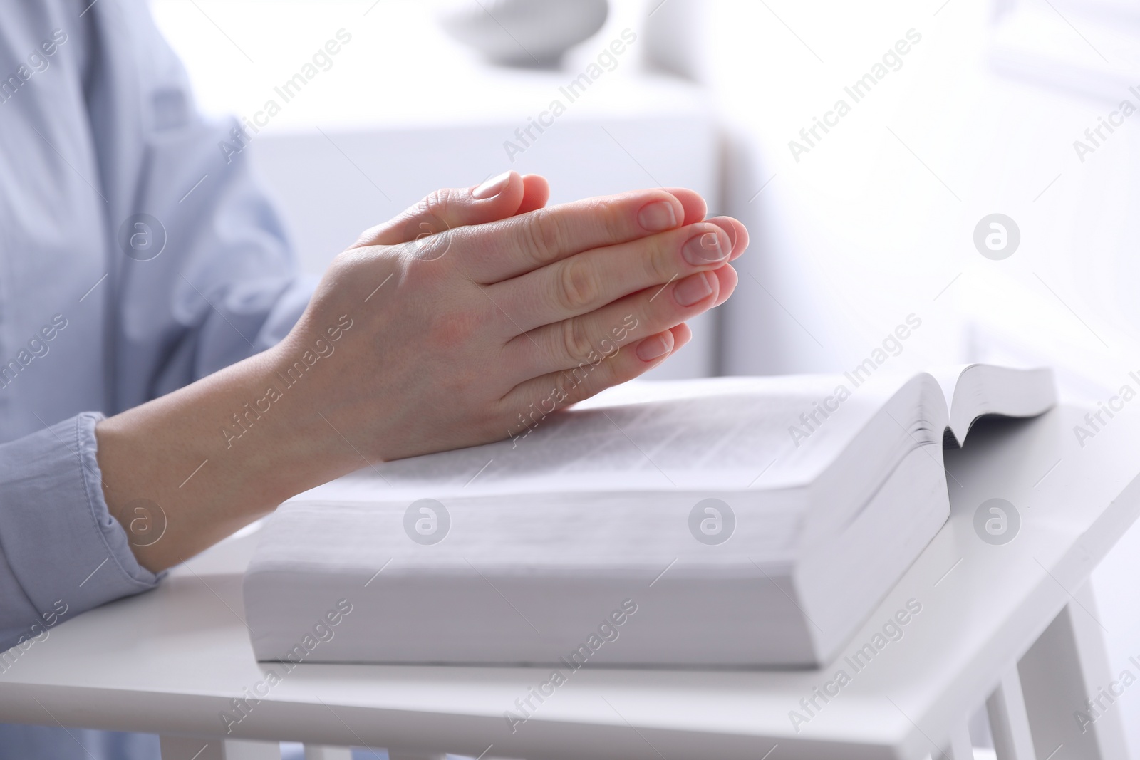 Photo of Religion. Christian woman praying over Bible indoors, closeup