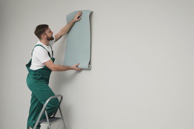 Photo of Worker hanging stylish wall paper sheet on light grey background. Space for text