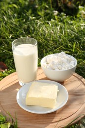 Photo of Wooden tray with tasty homemade butter and dairy products on grass outdoors