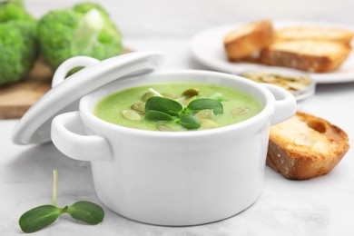Delicious broccoli cream soup with pumpkin seeds on white marble table, closeup