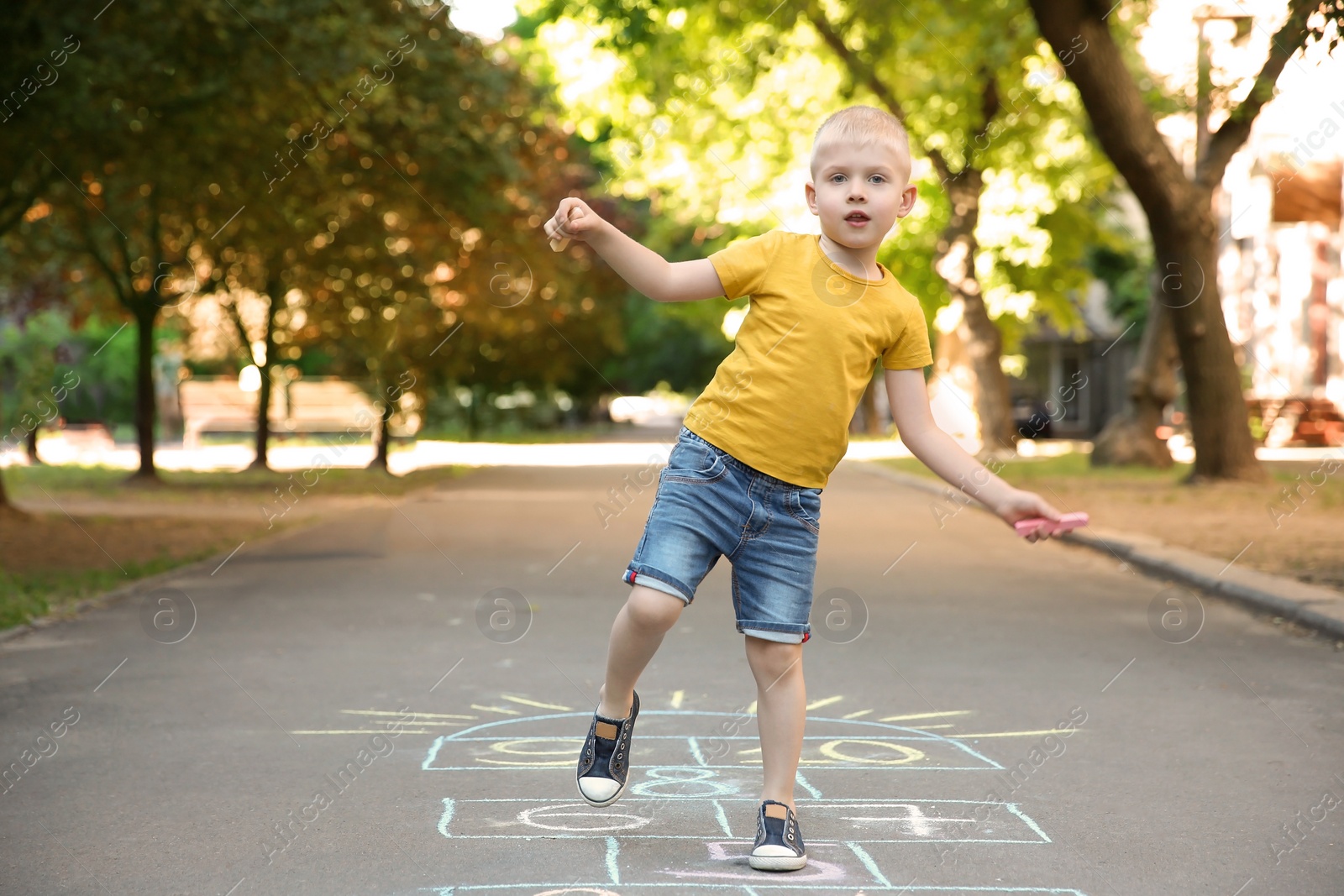 Photo of Little child playing hopscotch drawn with colorful chalk on asphalt