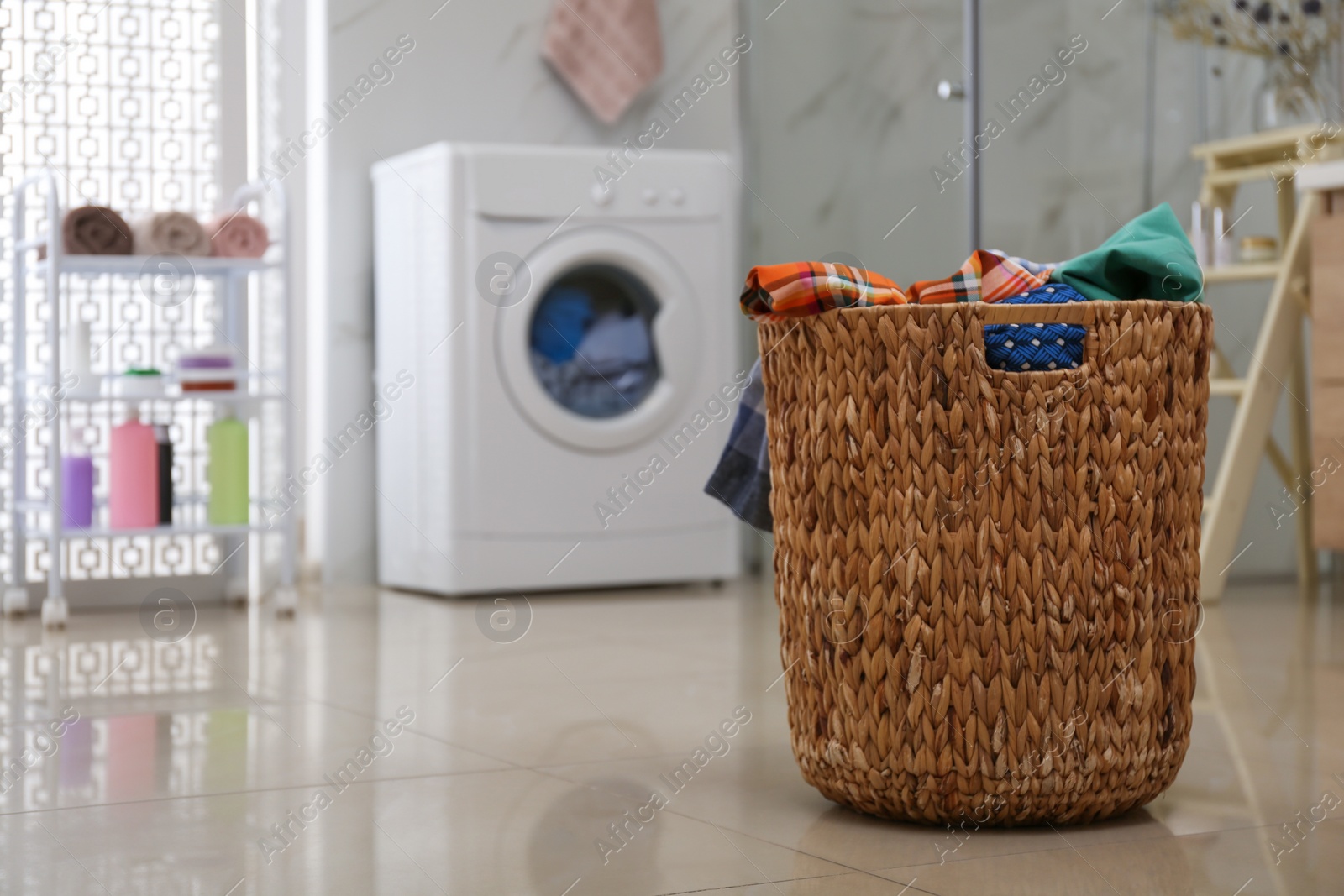 Photo of Wicker laundry basket full of different clothes on floor in bathroom