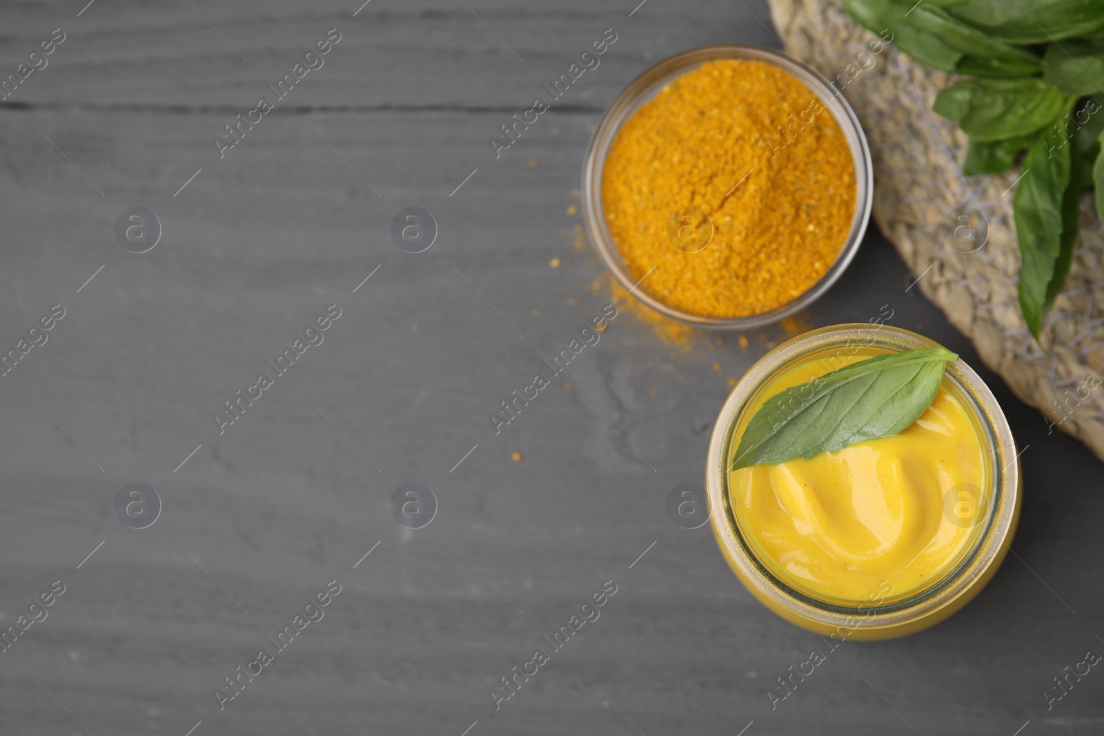 Photo of Tasty curry sauce, powder and basil leaves on grey wooden table, flat lay. Space for text