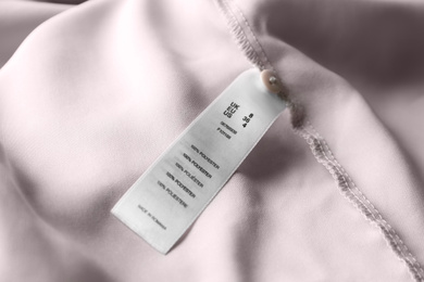 Photo of Clothing label with size and content information on light garment, closeup