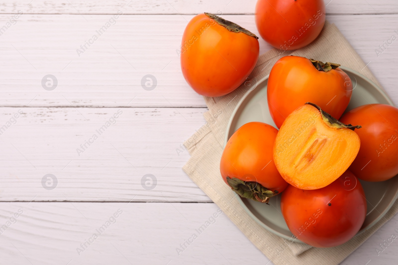 Photo of Delicious ripe juicy persimmons on white wooden table, flat lay. Space for text