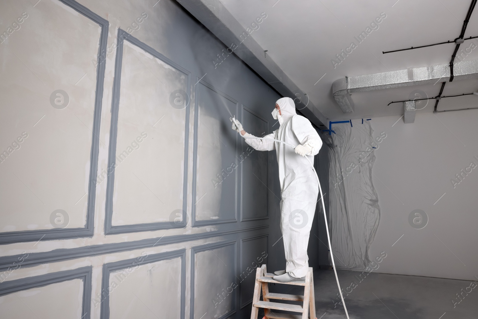 Photo of Decorator dyeing wall in grey color with spray paint indoors