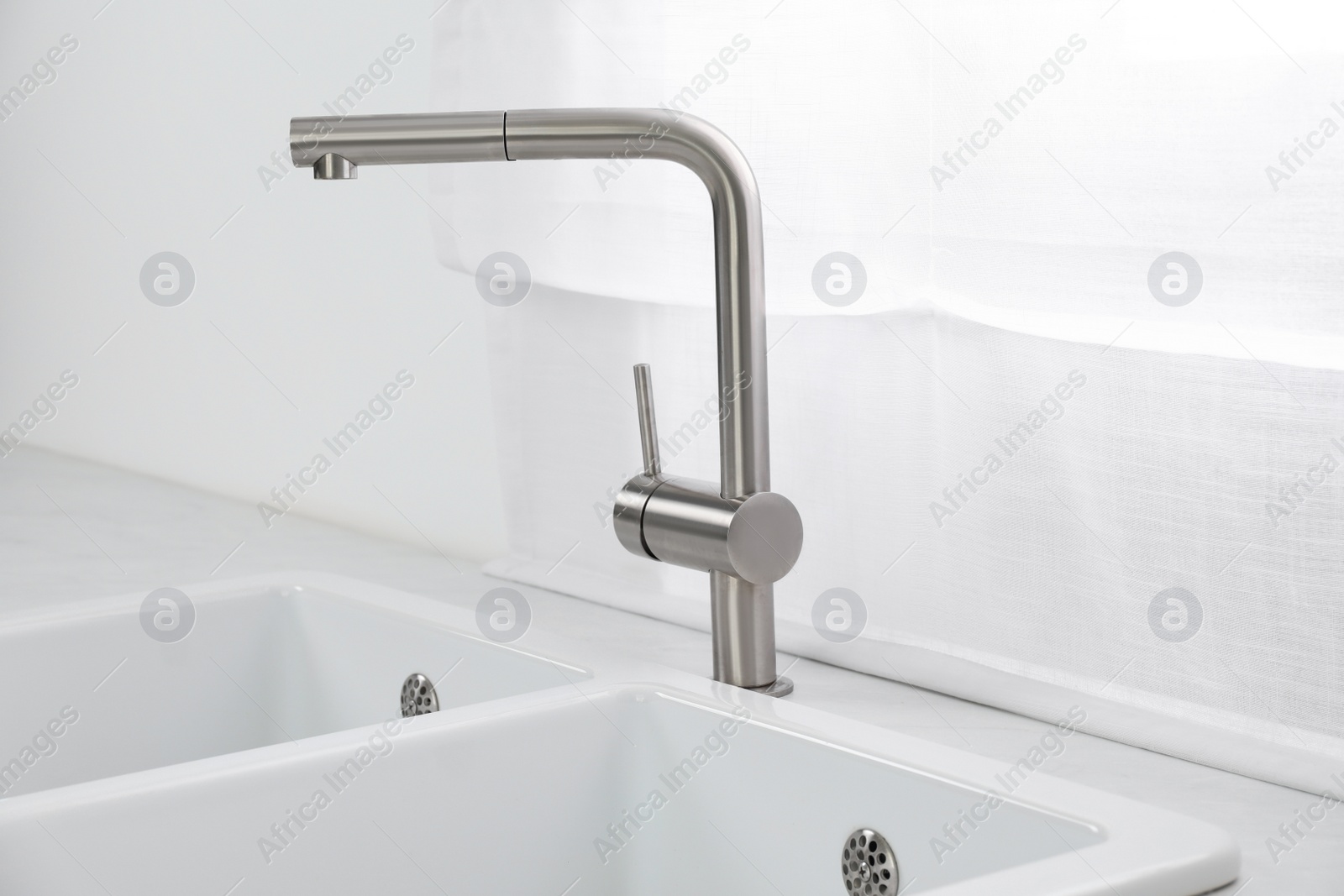 Photo of Modern sink and water tap near window in kitchen. Interior design