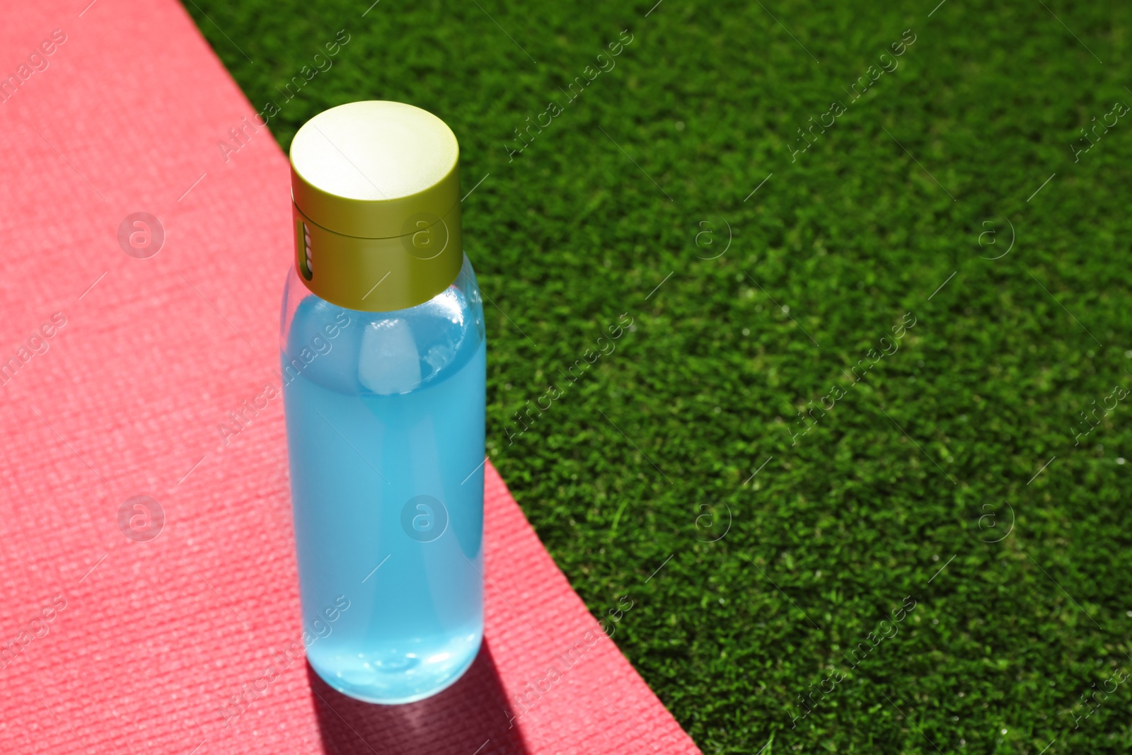 Photo of Bottle of light blue drink and mat on green grass, space for text