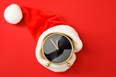 Photo of Alarm clock with Santa hat on red background, top view. New Year countdown