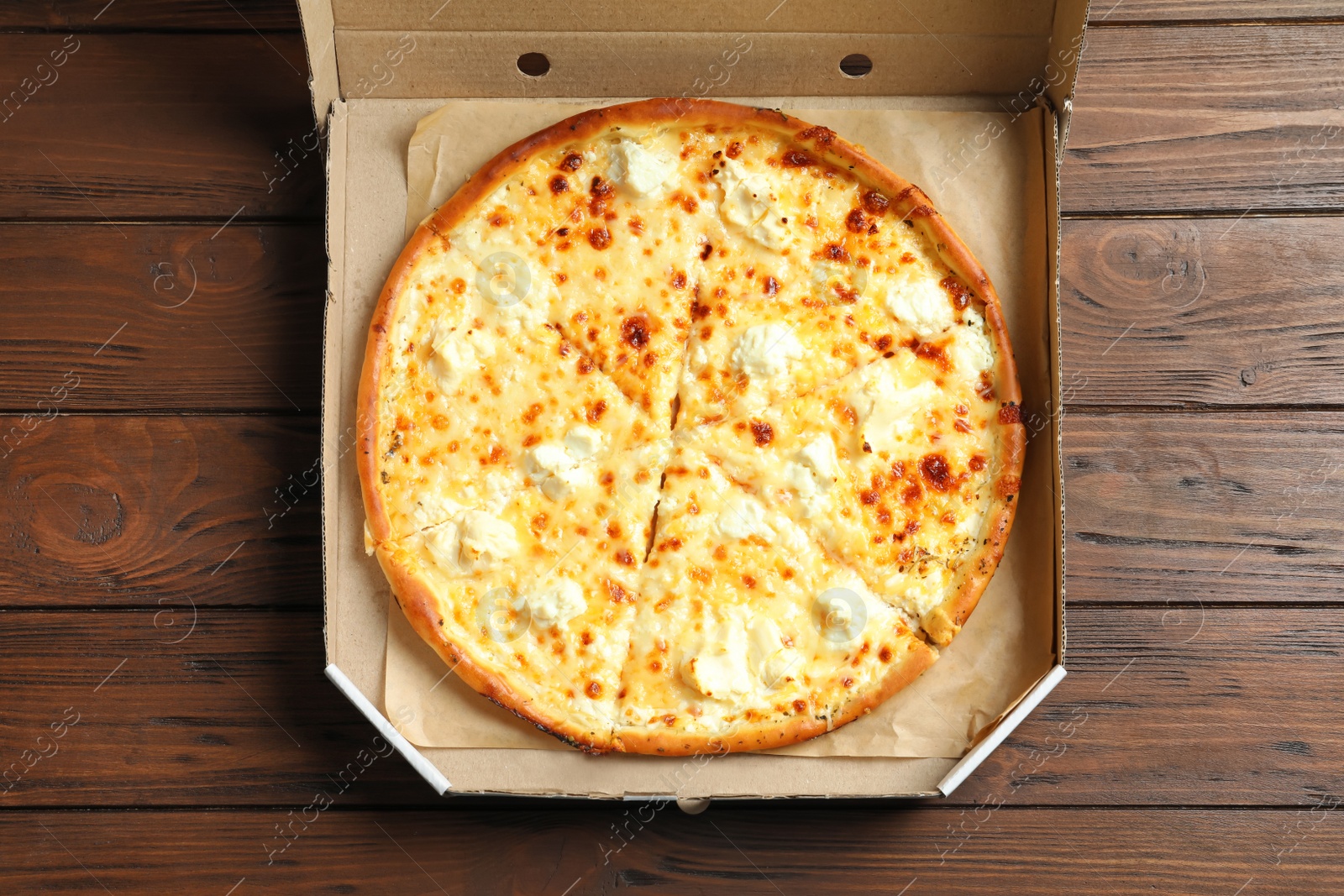 Photo of Carton box with delicious pizza on wooden background, top view