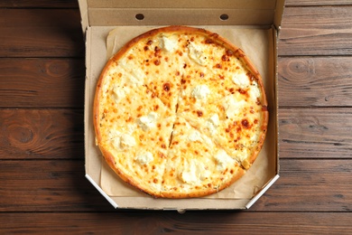 Photo of Carton box with delicious pizza on wooden background, top view