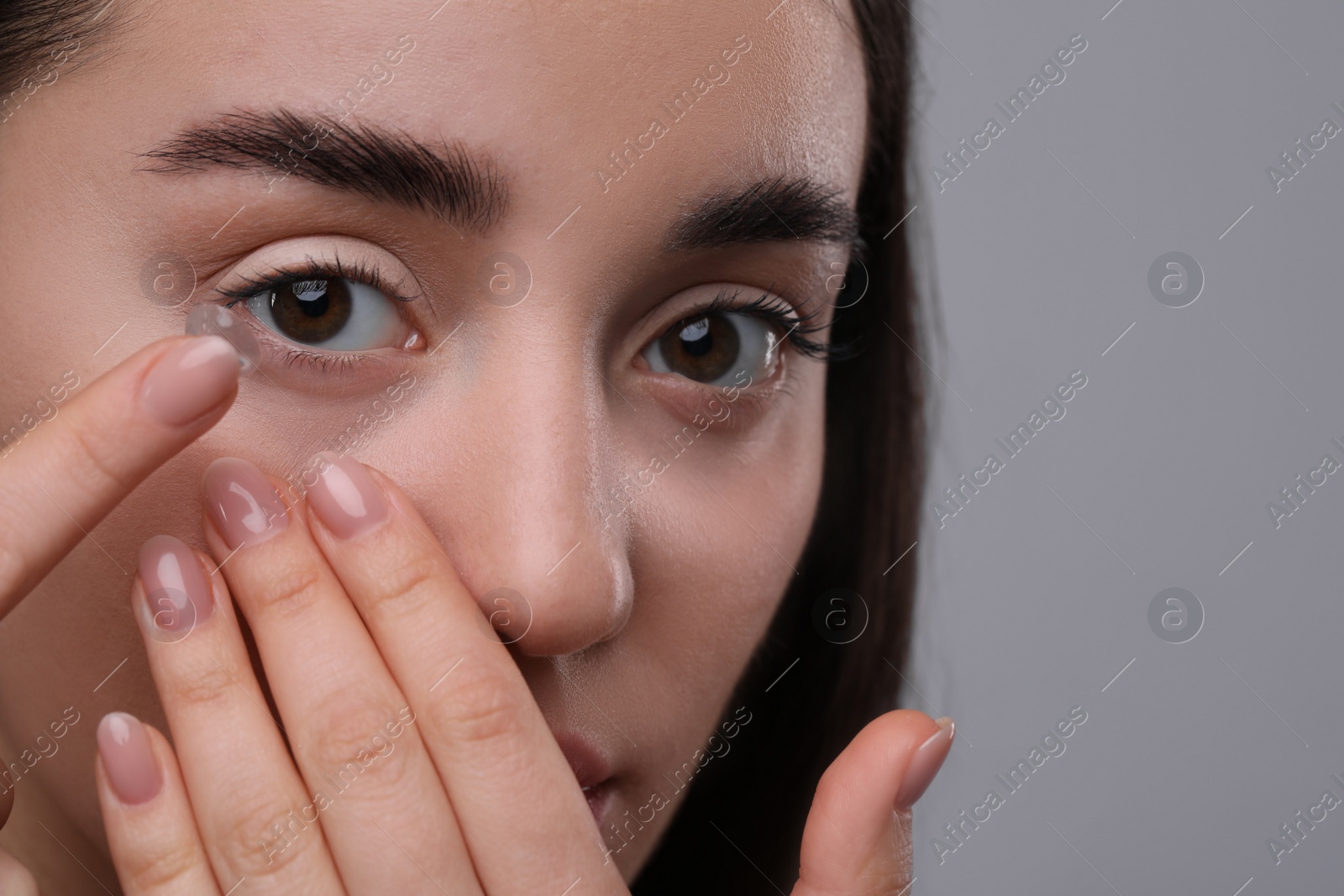 Photo of Closeup view of young woman putting in contact lens on grey background