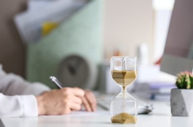 Hourglass and woman working on background. Time management