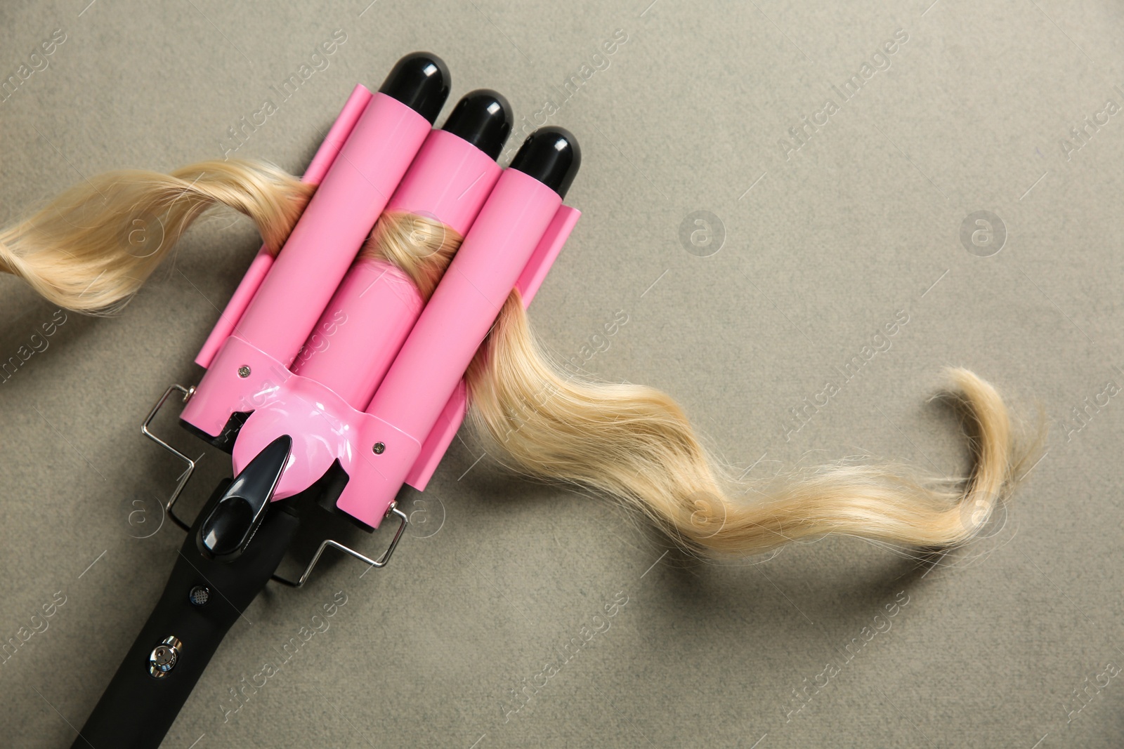 Photo of Modern triple curling iron and blonde hair lock on grey background, top view