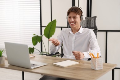 Photo of Man in headphones using video chat during webinar at wooden table in office