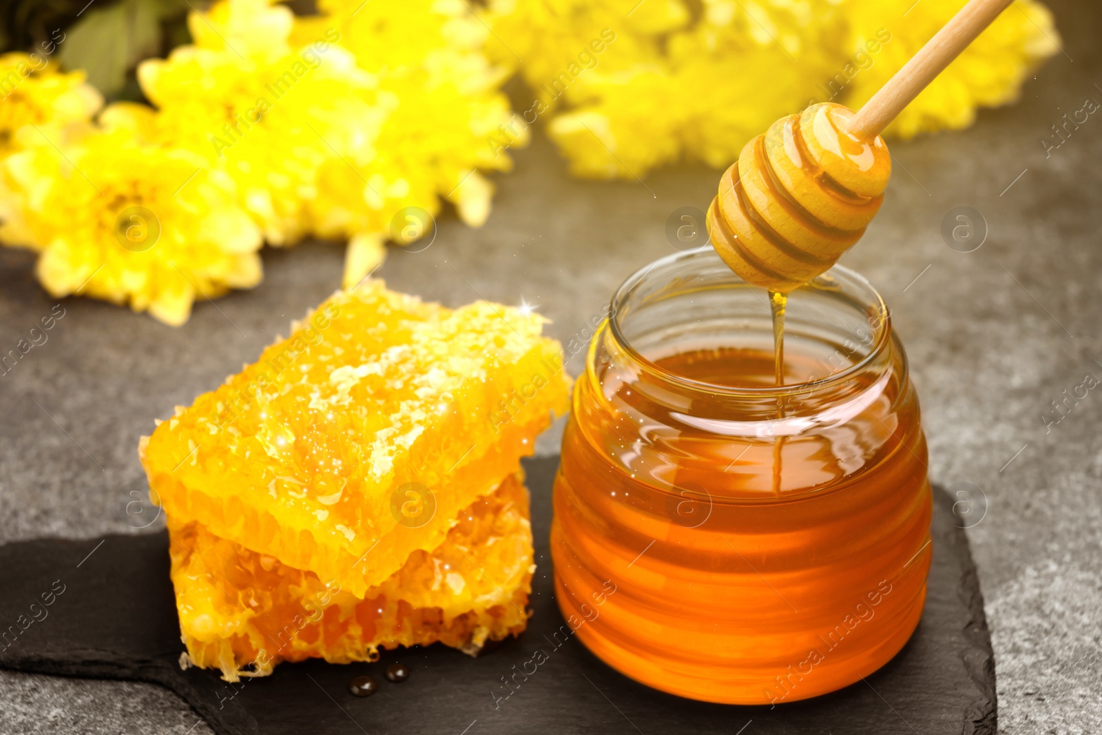 Image of Natural honey dripping from dipper into glass jar and honeycomb on table under sunlight