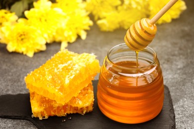 Natural honey dripping from dipper into glass jar and honeycomb on table under sunlight