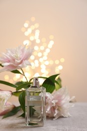Photo of Bottleperfume and beautiful lily flowers on table against beige background with blurred lights, space for text