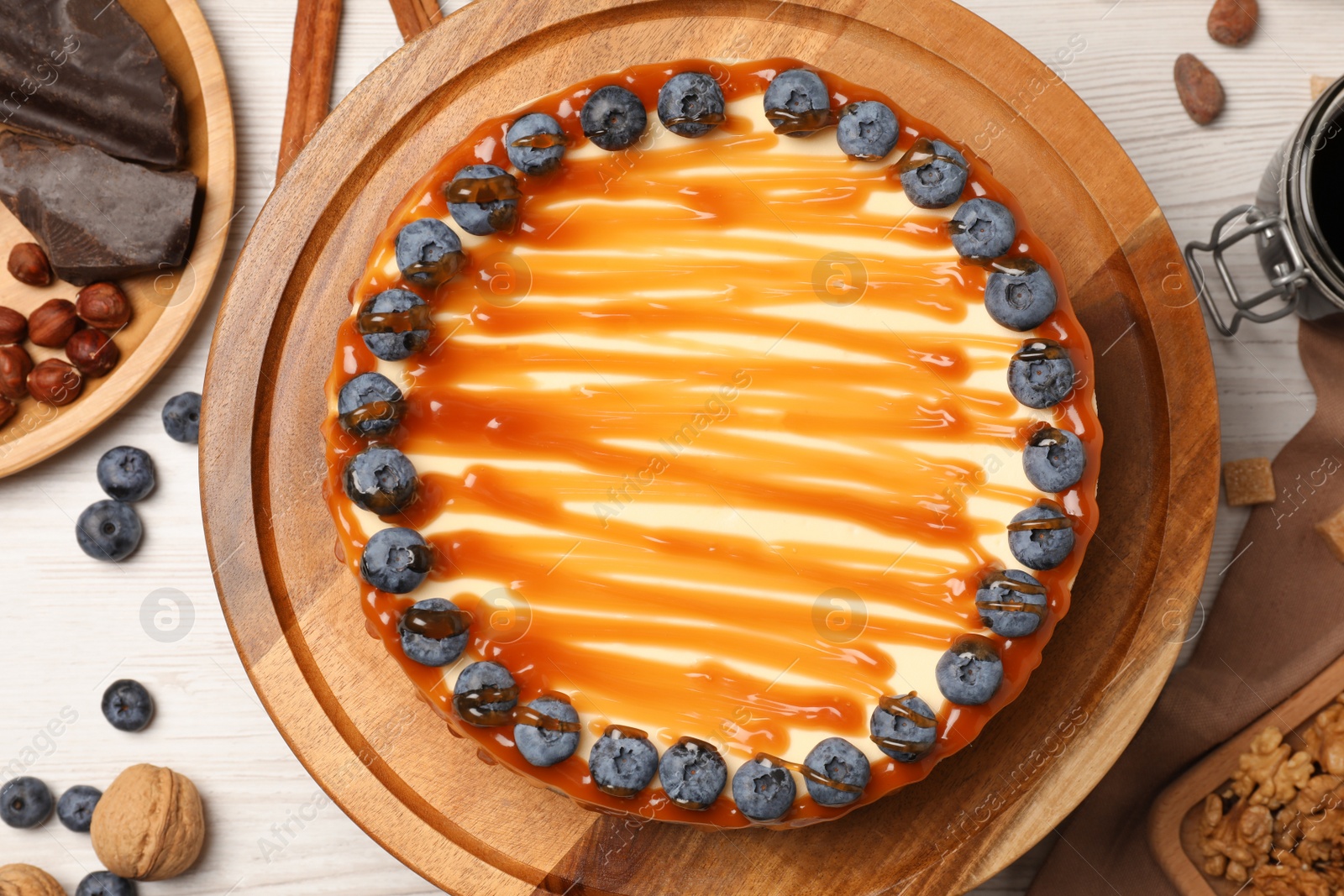 Photo of Delicious cheesecake with caramel and blueberries on white wooden table, flat lay