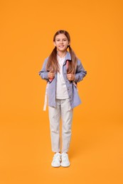 Photo of Happy schoolgirl with backpack on orange background