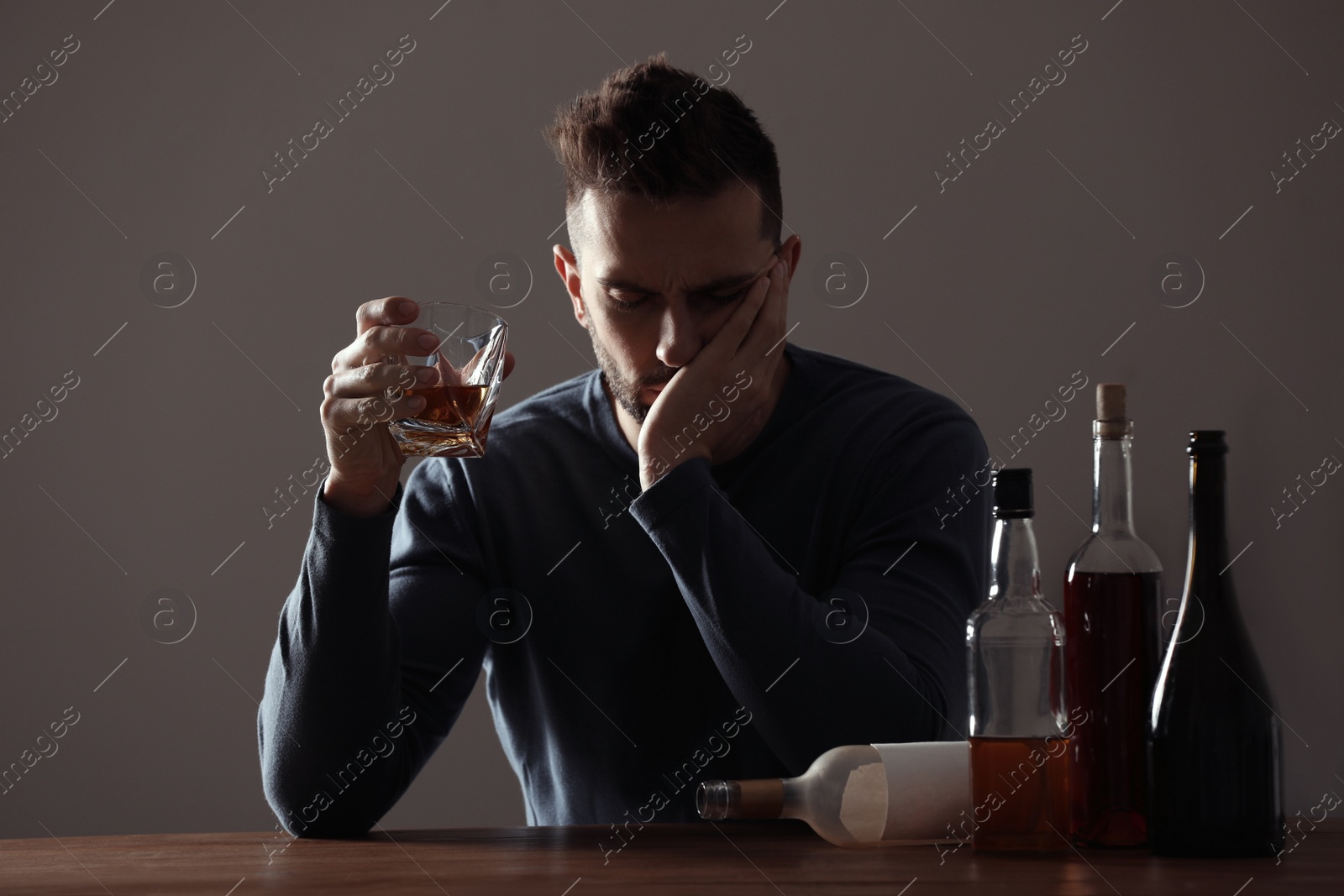 Photo of Addicted man with alcoholic drink at wooden table indoors