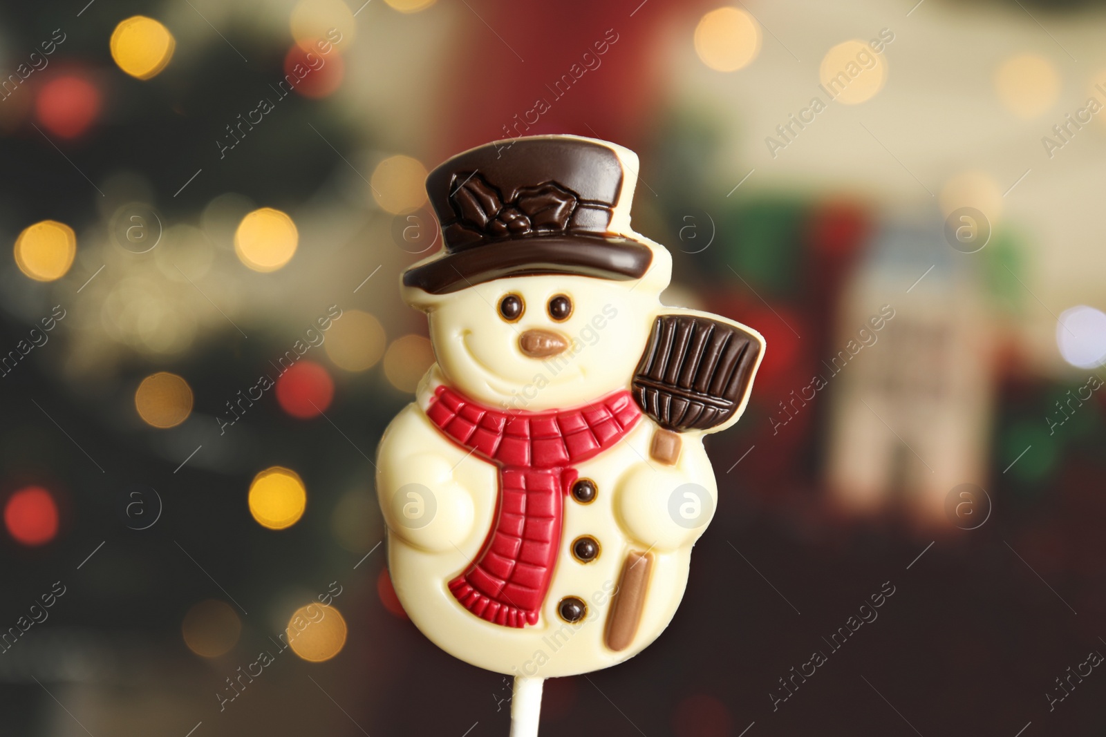 Photo of Funny chocolate snowman candy against blurred Christmas tree, closeup