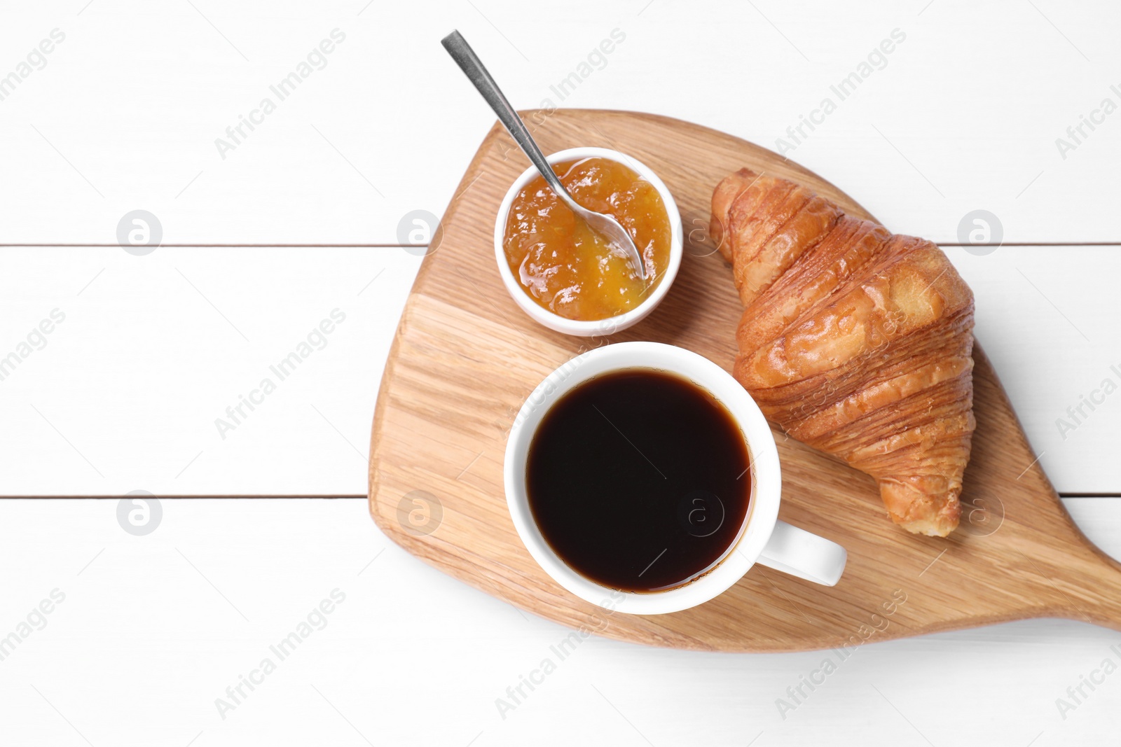 Photo of Tasty breakfast. Cup of coffee, jam and croissant on white wooden table, top view. Space for text