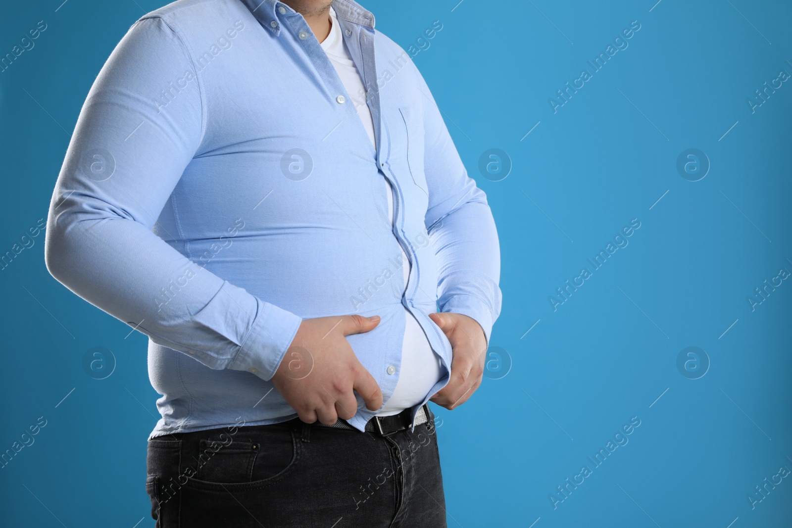 Photo of Overweight man in tight shirt on light blue background, closeup. Space for text