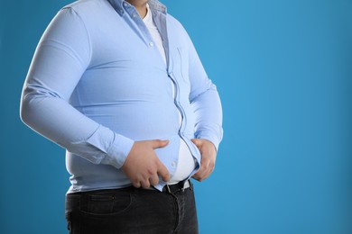 Photo of Overweight man in tight shirt on light blue background, closeup. Space for text