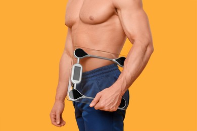 Photo of Athletic man holding scales on orange background, closeup. Weight loss concept