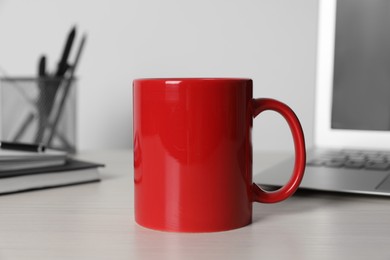 Photo of Red ceramic mug, laptop and stationery on white table at workspace