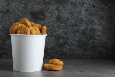 Photo of Bucket with tasty chicken nuggets on grey table. Space for text