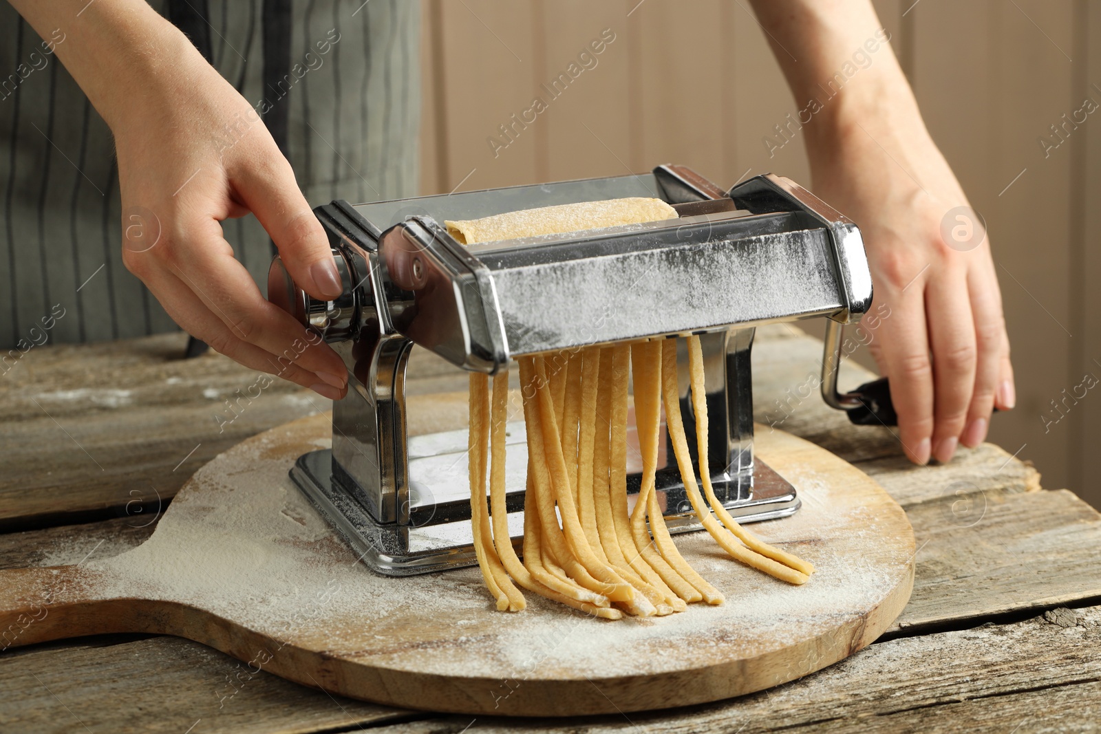 Photo of Woman making homemade noodles with pasta maker at wooden table, closeup