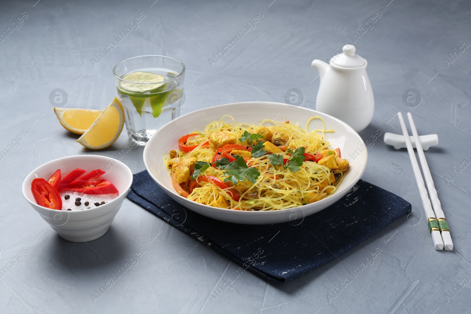 Photo of Stir-fry. Delicious cooked noodles with chicken and vegetables in bowl served on gray textured table