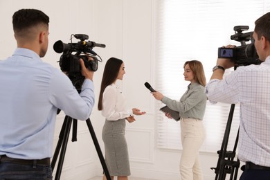 Photo of Professional journalist interviewing young business woman and cameramen shooting video for broadcast