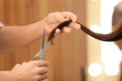 Barber making stylish haircut with professional scissors in beauty salon, closeup