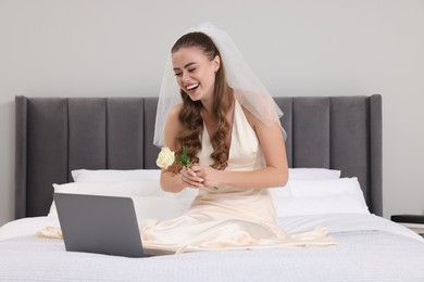 Happy bride with rose and laptop on bed in bedroom