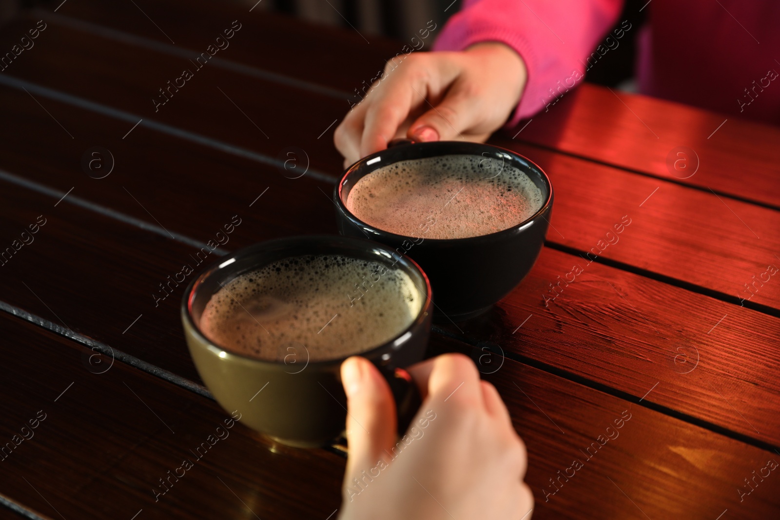 Photo of Women with cups of hot coffee at wooden table, closeup